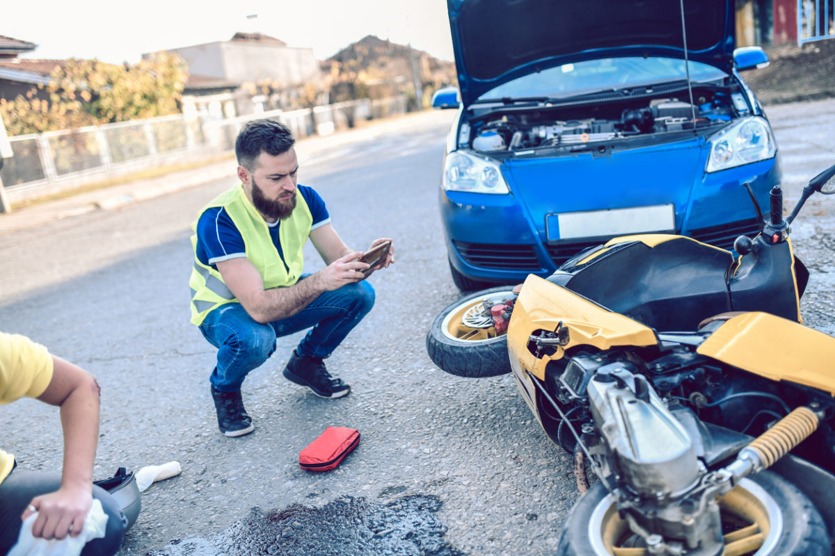 man taking pictures of an accident scene involving a car and scooter